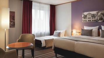 Una habitación de hotel con una cama, dos mesitas de noche, una silla, una pequeña mesa y un ventanal con cortinas.