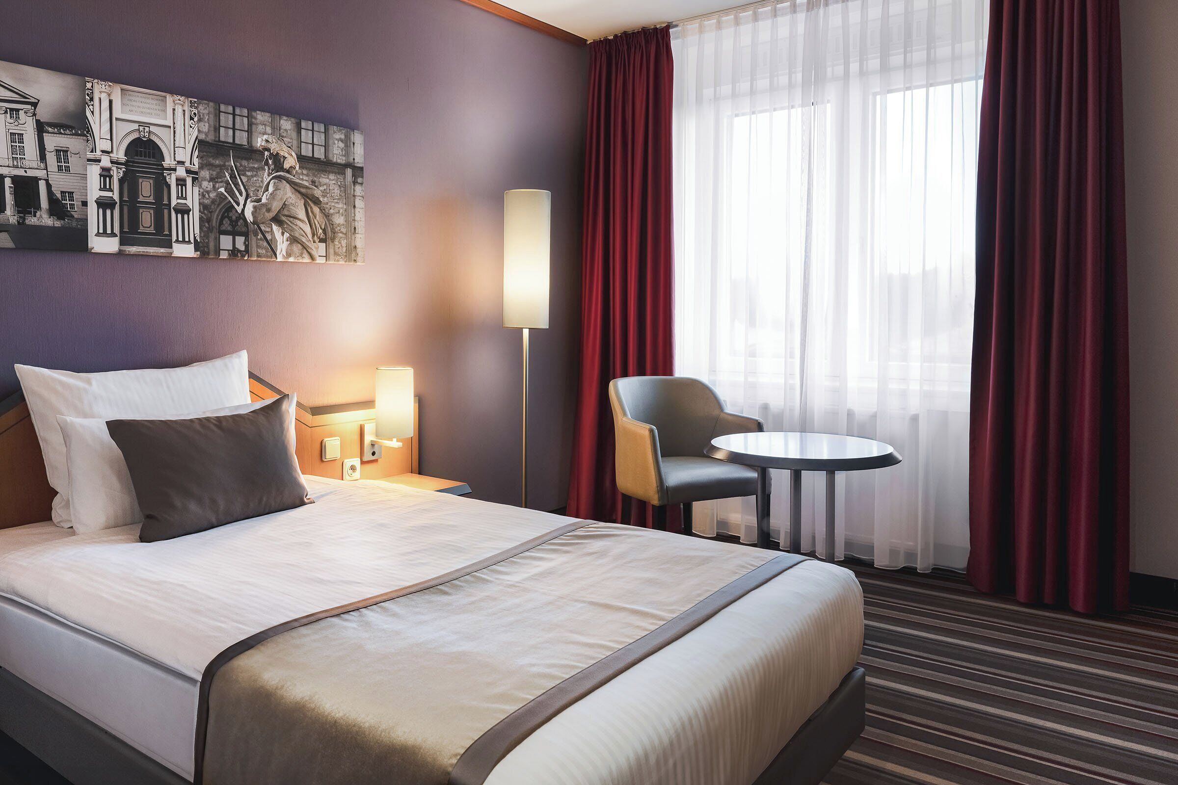 Una habitación de hotel con una cama grande, un escritorio con una silla, una mesita redonda y un cuadro en la pared.