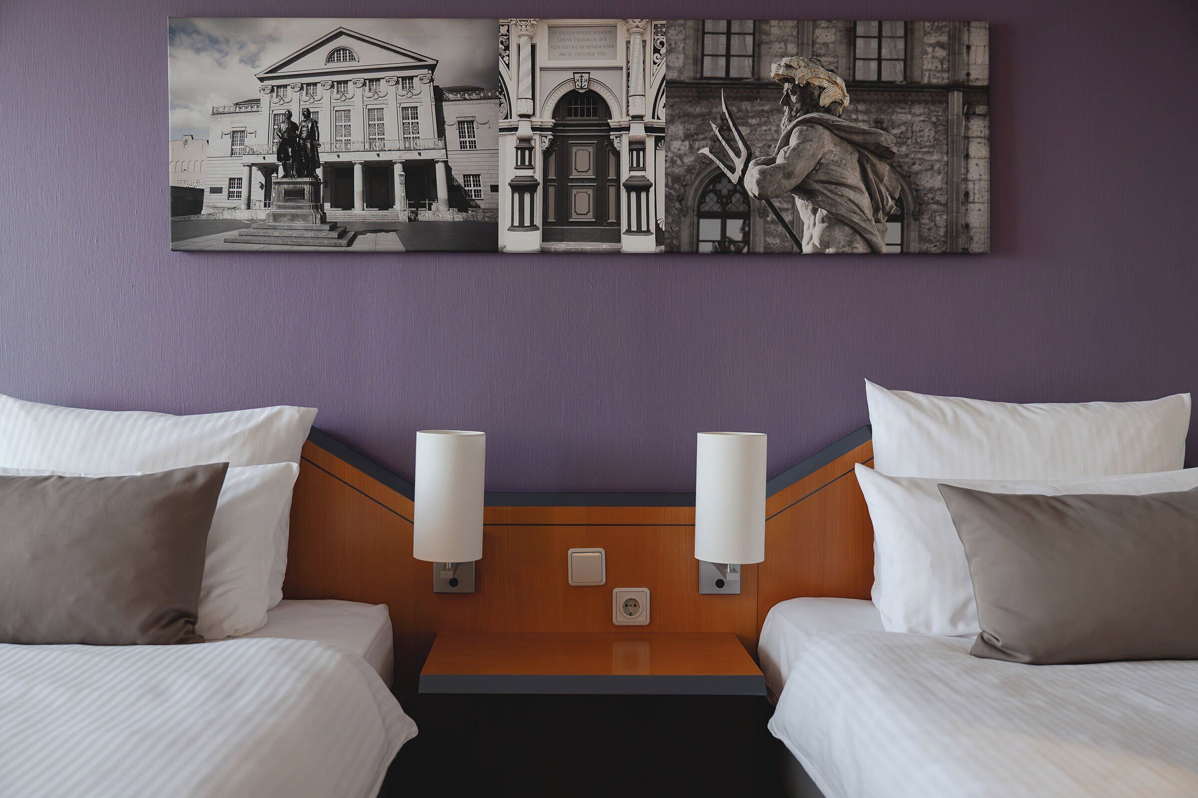 A hotel room with two beds, a headboard with wall sconces, and a large framed artwork above the beds.
