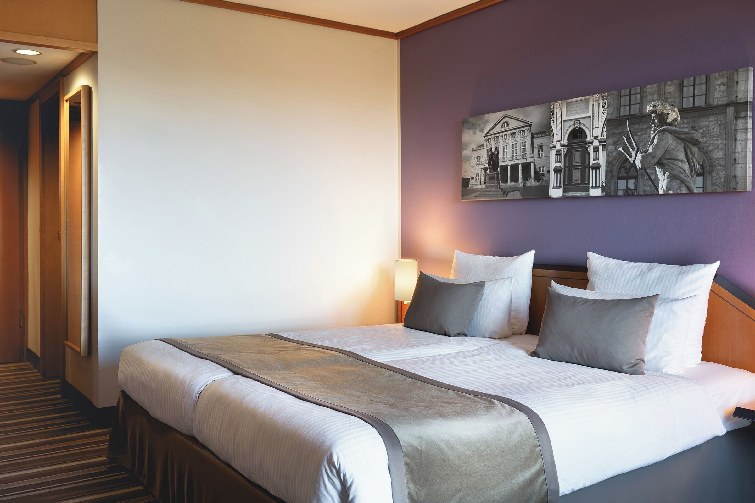 A hotel room with a large bed, a headboard, a nightstand, a lamp, and a painting on the wall.