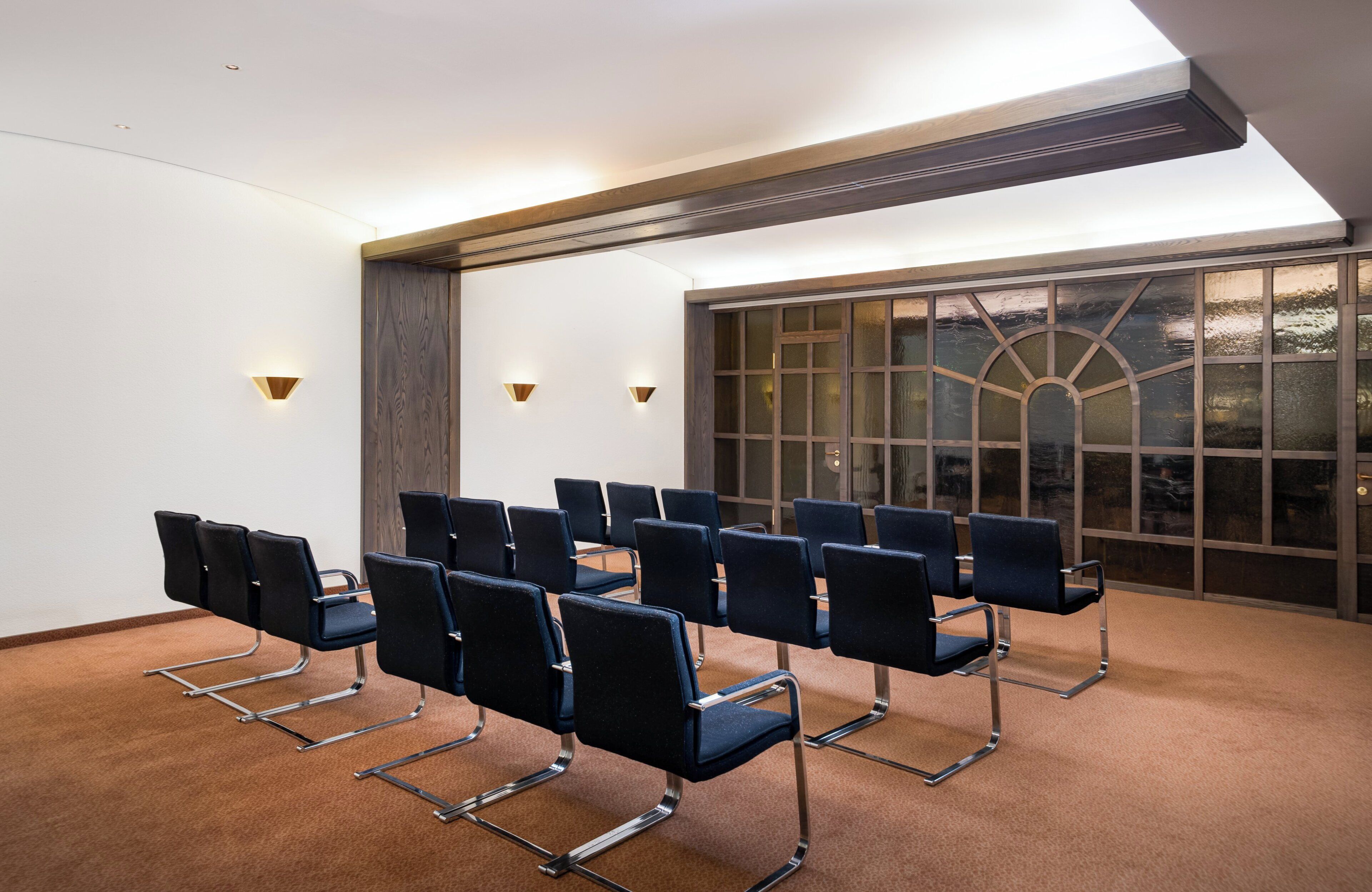 Un salón de conferencias con filas de sillas, un ventanal con vistas e iluminación empotrada en la pared.