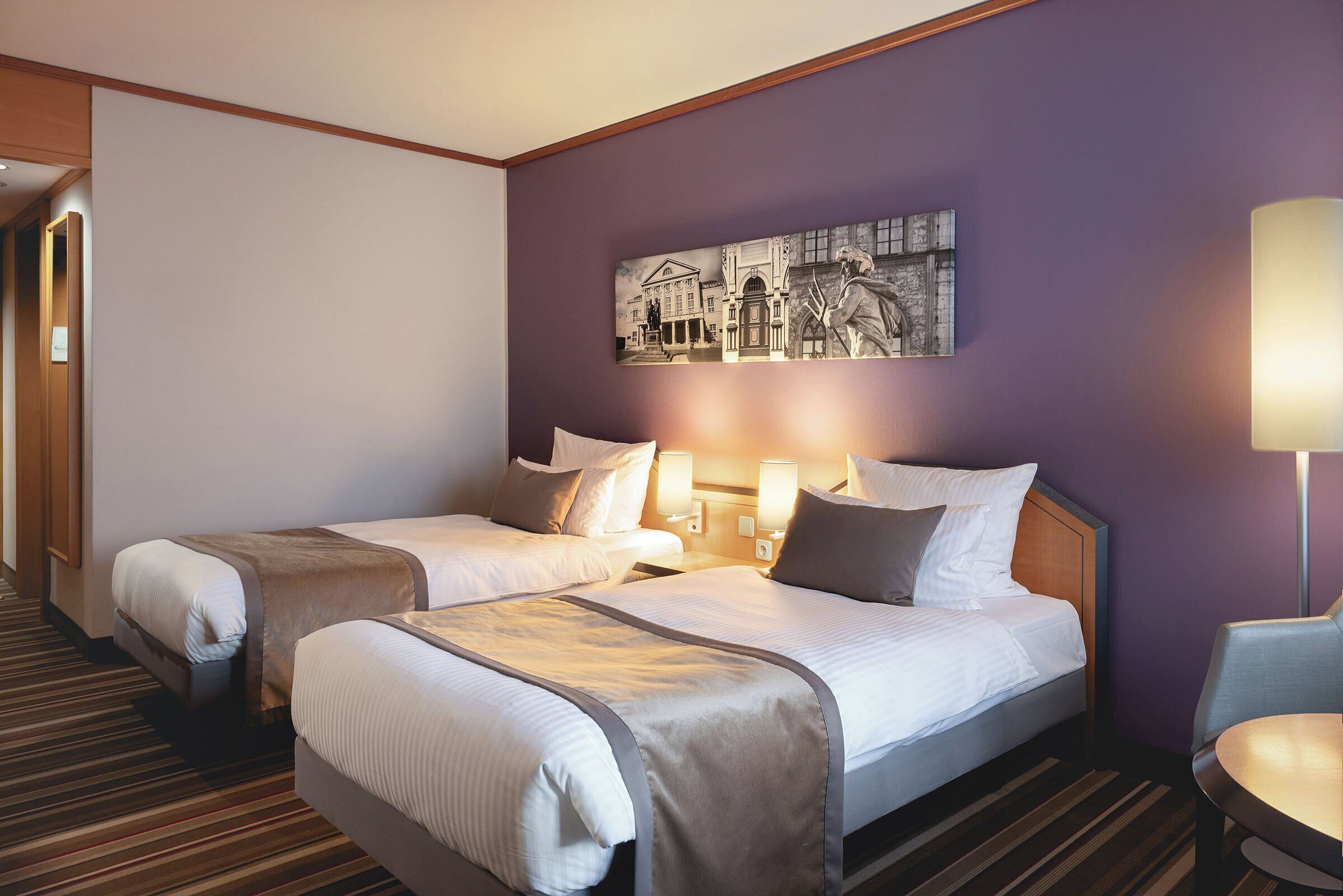 A hotel room with two beds, a large wall painting, and a lamp.