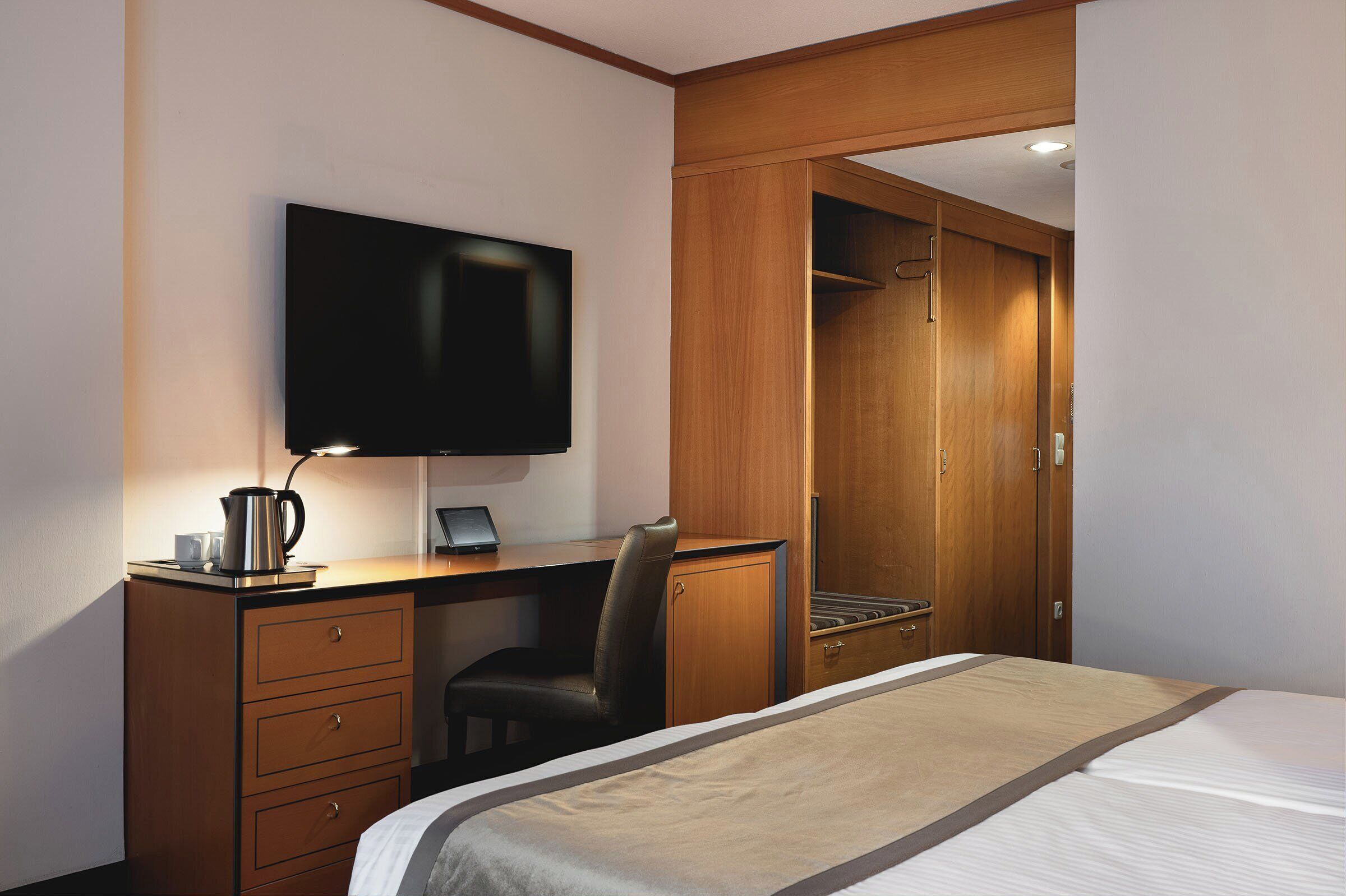Habitación de hotel con cama, escritorio con computadora, televisor y armario.