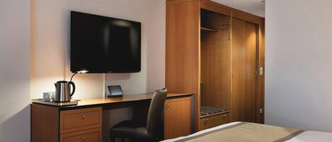 A hotel room with a bed, a desk with a computer, a television, and a wardrobe.