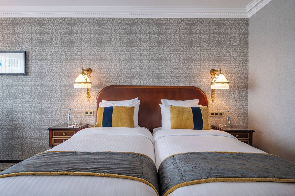 A double bed with two nightstands, a wooden headboard, and two wall-mounted lamps.