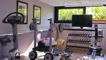 Un gimnasio con equipo de ejercicio, un televisor y una ventana con vistas a la vegetación.