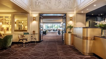 Een hotel lobby met een geometrisch patroon vloerkleed, een receptiebalie en klassieke wandreliëfs.