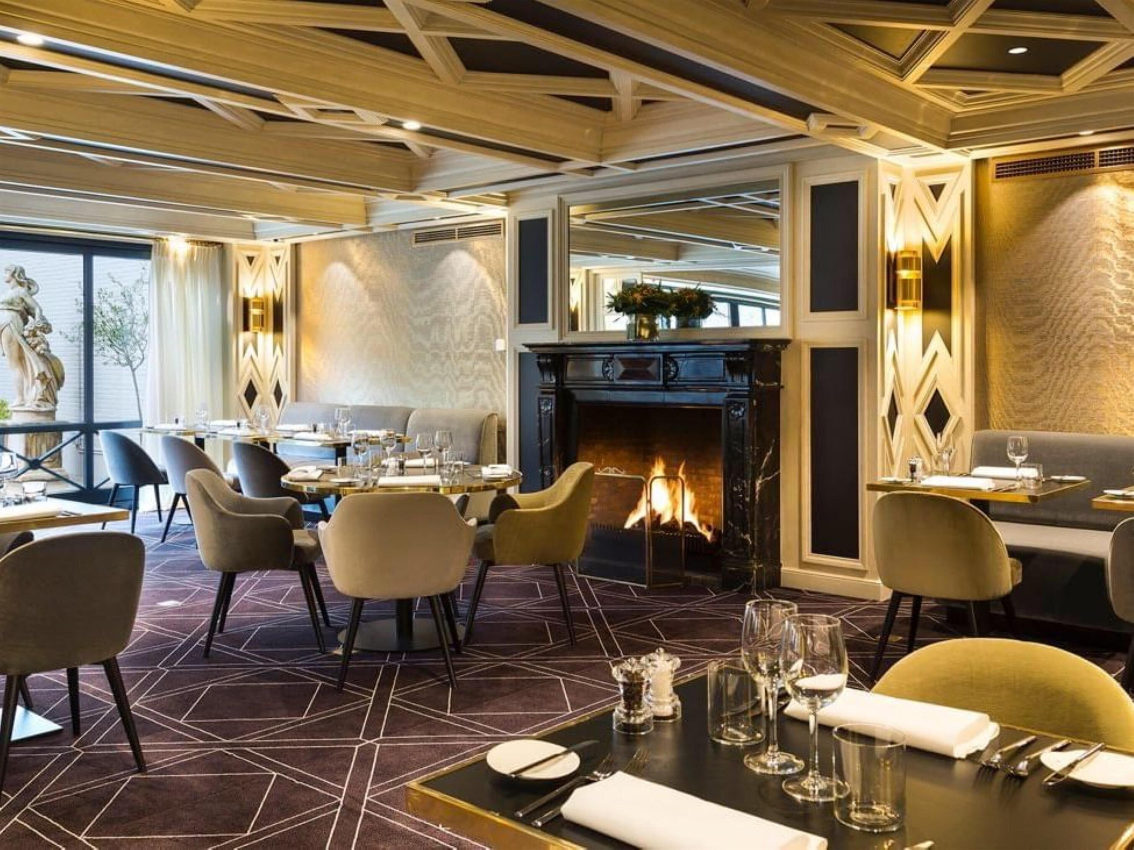 A restaurant with a fireplace, dining tables, chairs, and a patterned floor.