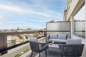 En balkon med to stole og et bord, der udover en byudsigt.