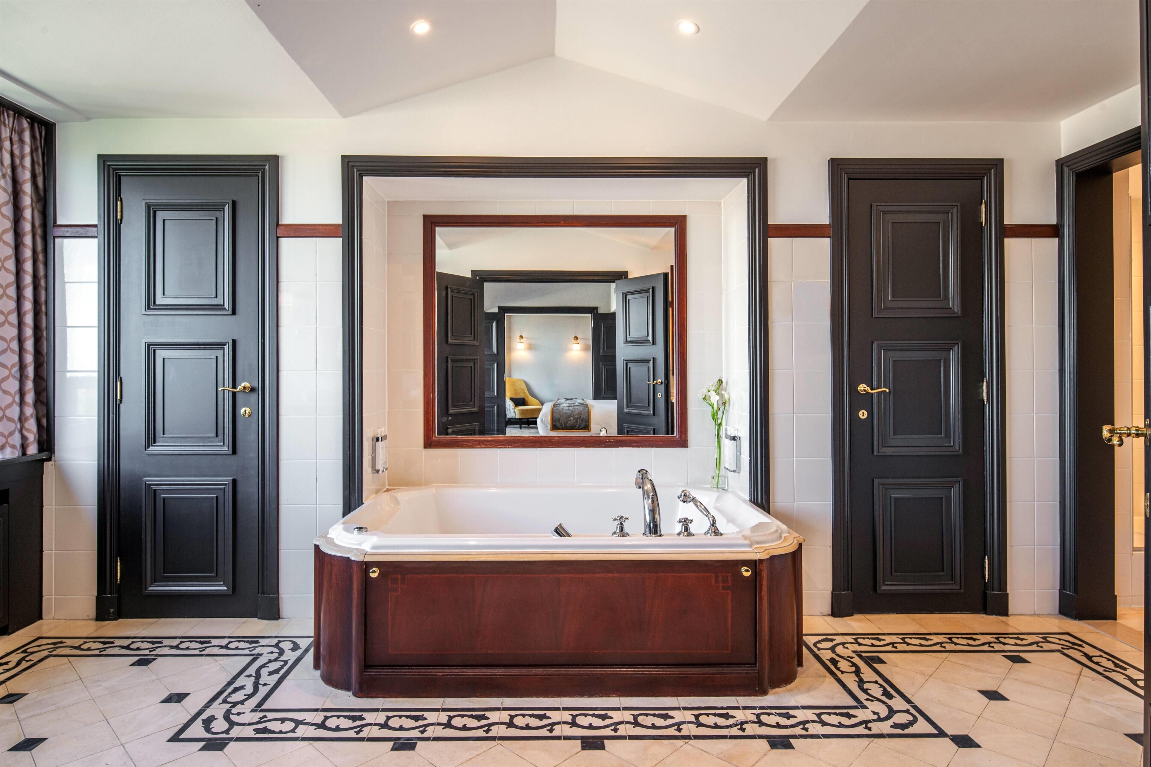 A bathroom with a large freestanding bathtub, a mirror, and two doors.
