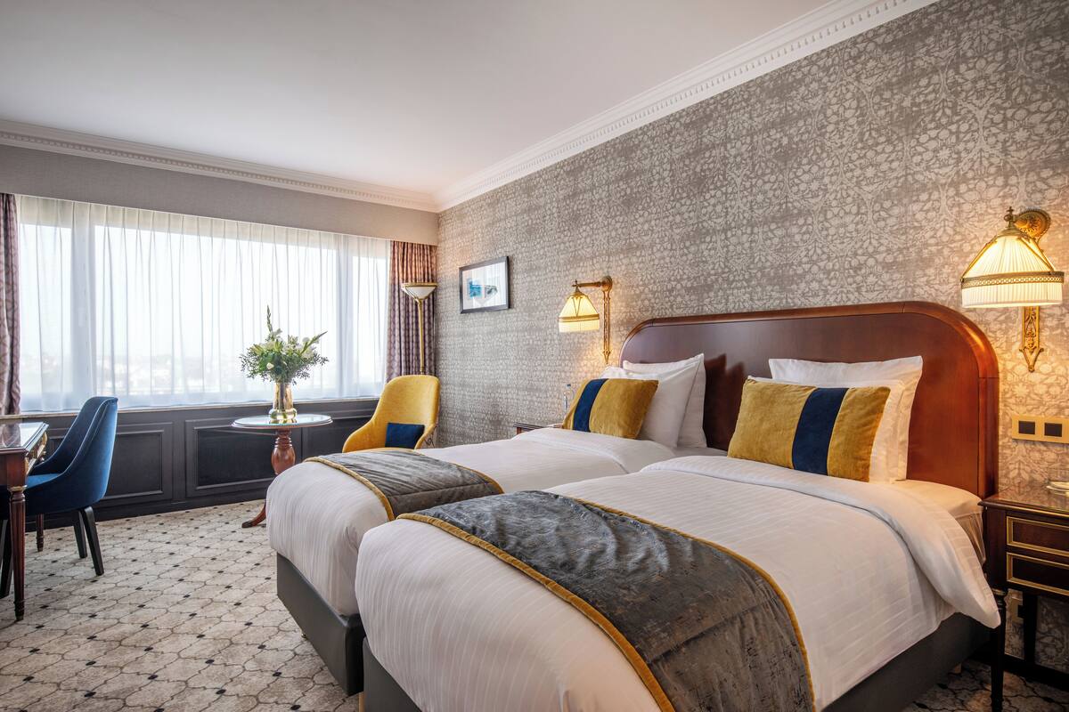 A hotel room with two beds, a desk, a chair, and a window with curtains.