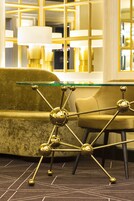 A modern interior with a gold-colored sofa, a glass-top coffee table with a metallic base, and a patterned carpet.