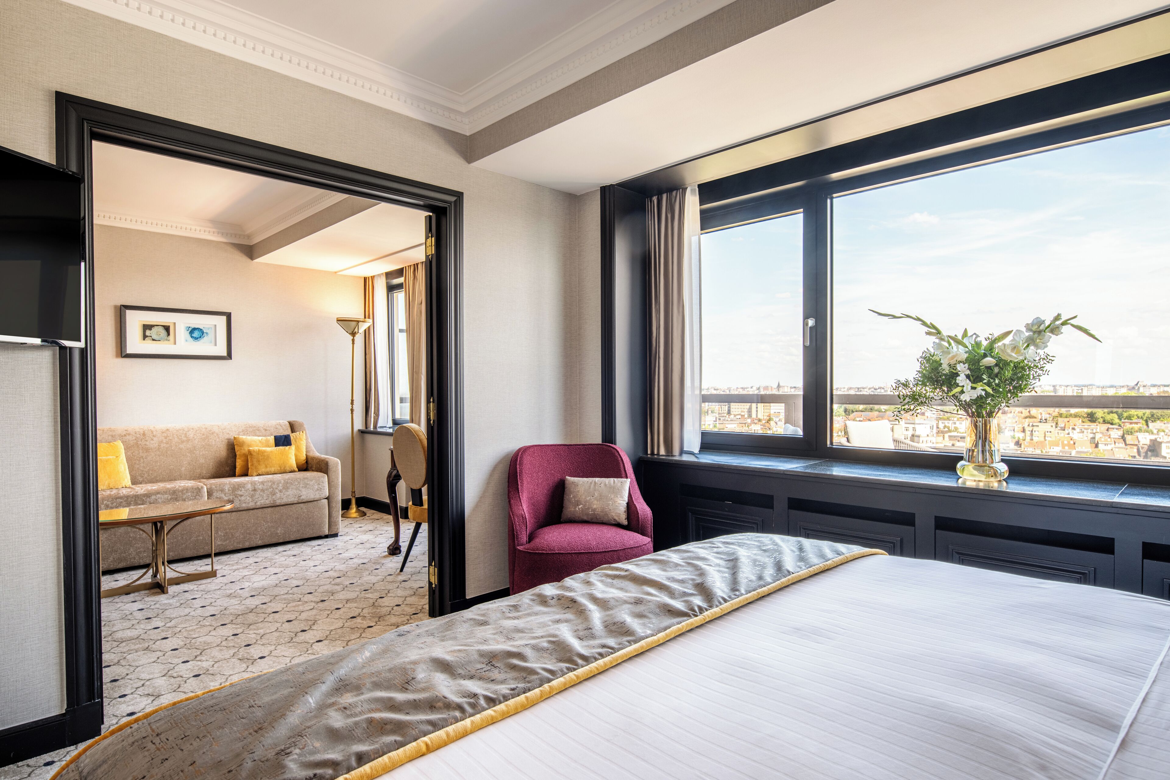 A hotel room with a bed, a sofa, a chair, and a window with a city view.
