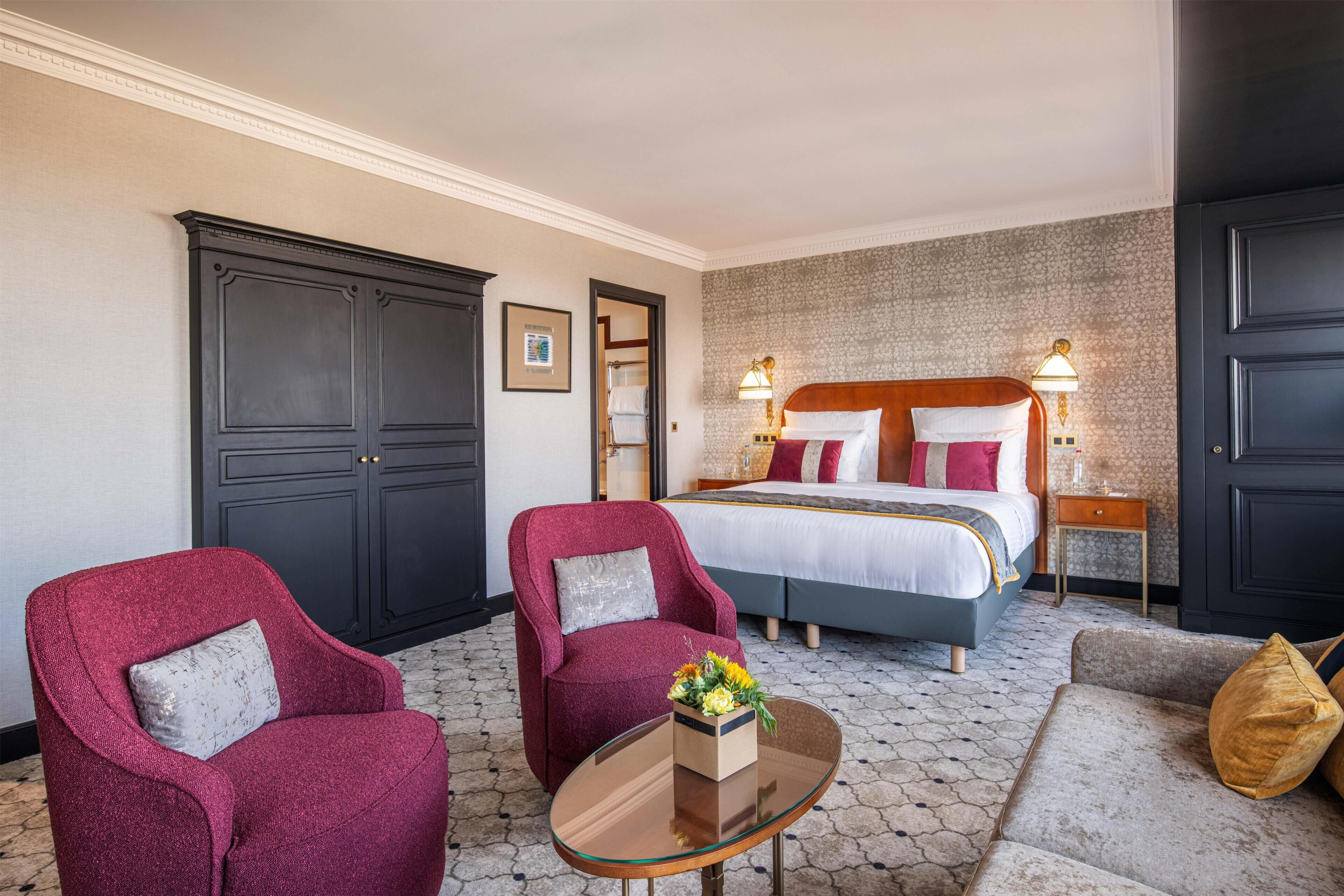 Una camera d'albergo con un letto grande, due poltrone, un tavolino in vetro e un divano.
