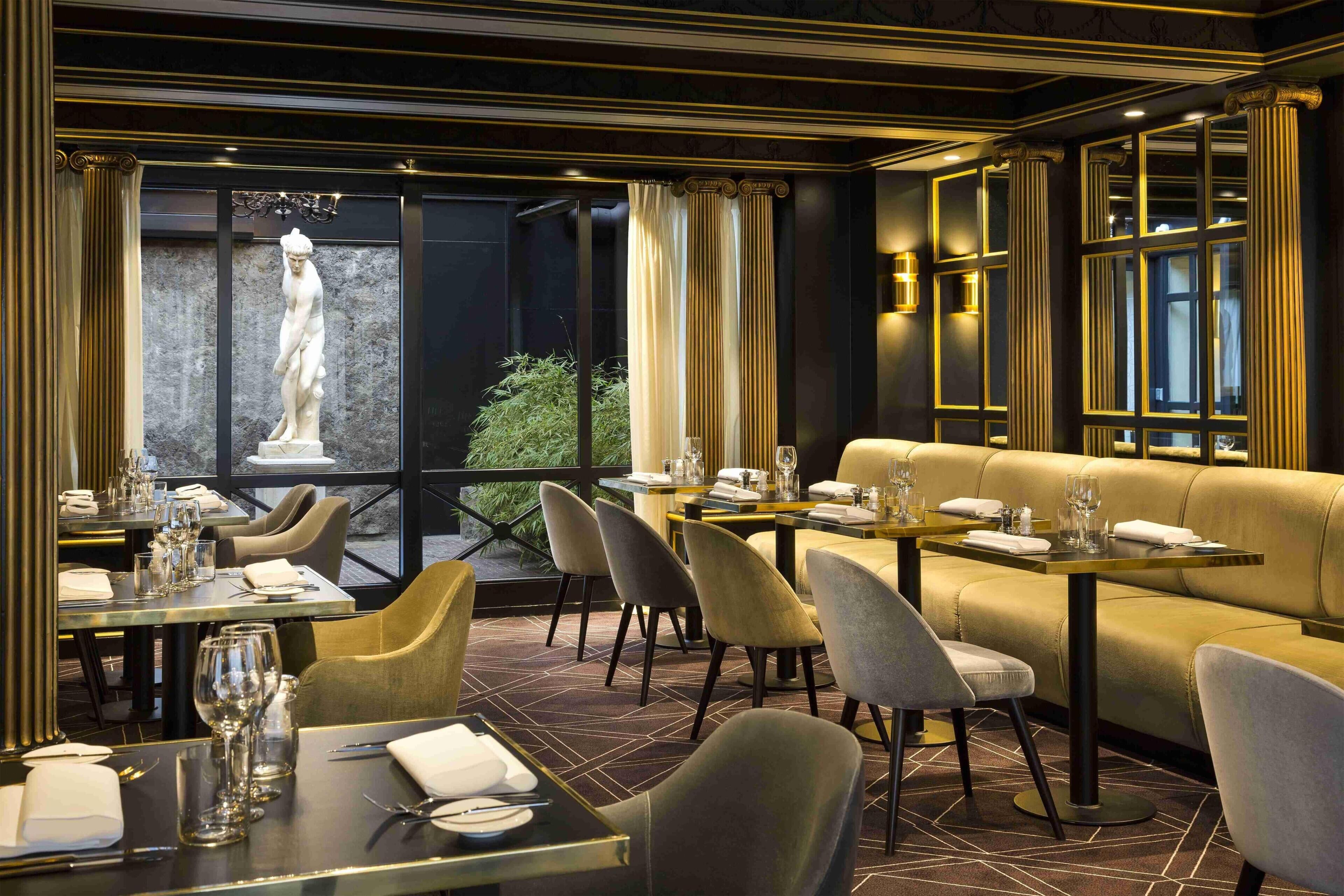 Een restaurantinterieur met een eetgedeelte, een bank en een beeld op de achtergrond.
