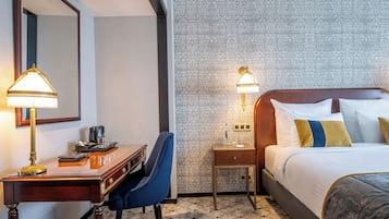 Une chambre d’hôtel avec un lit, un bureau avec une lampe, une chaise, une table de chevet et un papier peint à motifs.