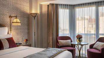 Habitación de hotel con cama, dos sillones, una mesita con un florero y una lámpara de pie.