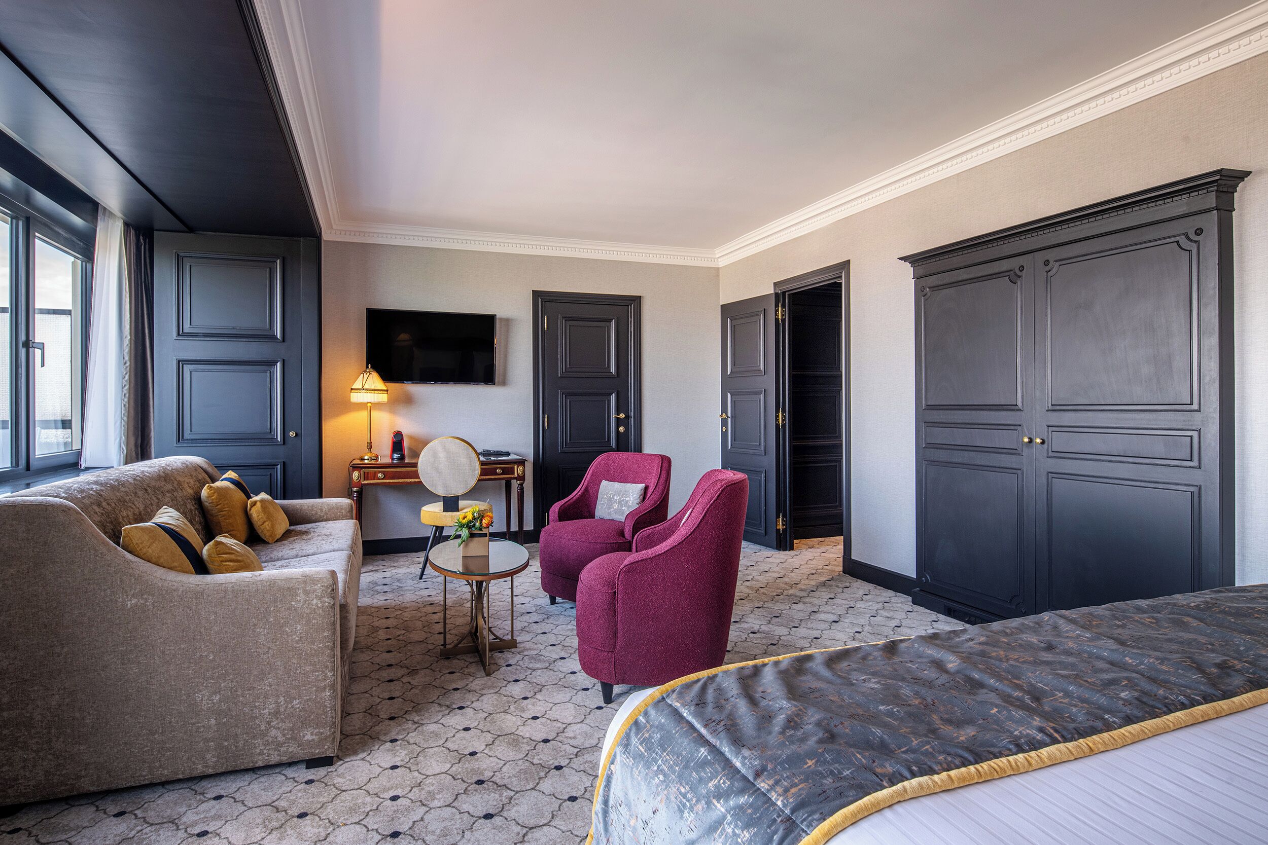 A hotel room with a bed, a sofa, a chair, a desk, and a TV.
