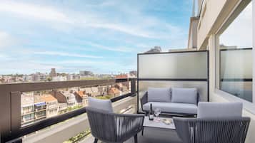 A balcony with a sofa and chairs, a table with a bottle and glasses, and a city view.