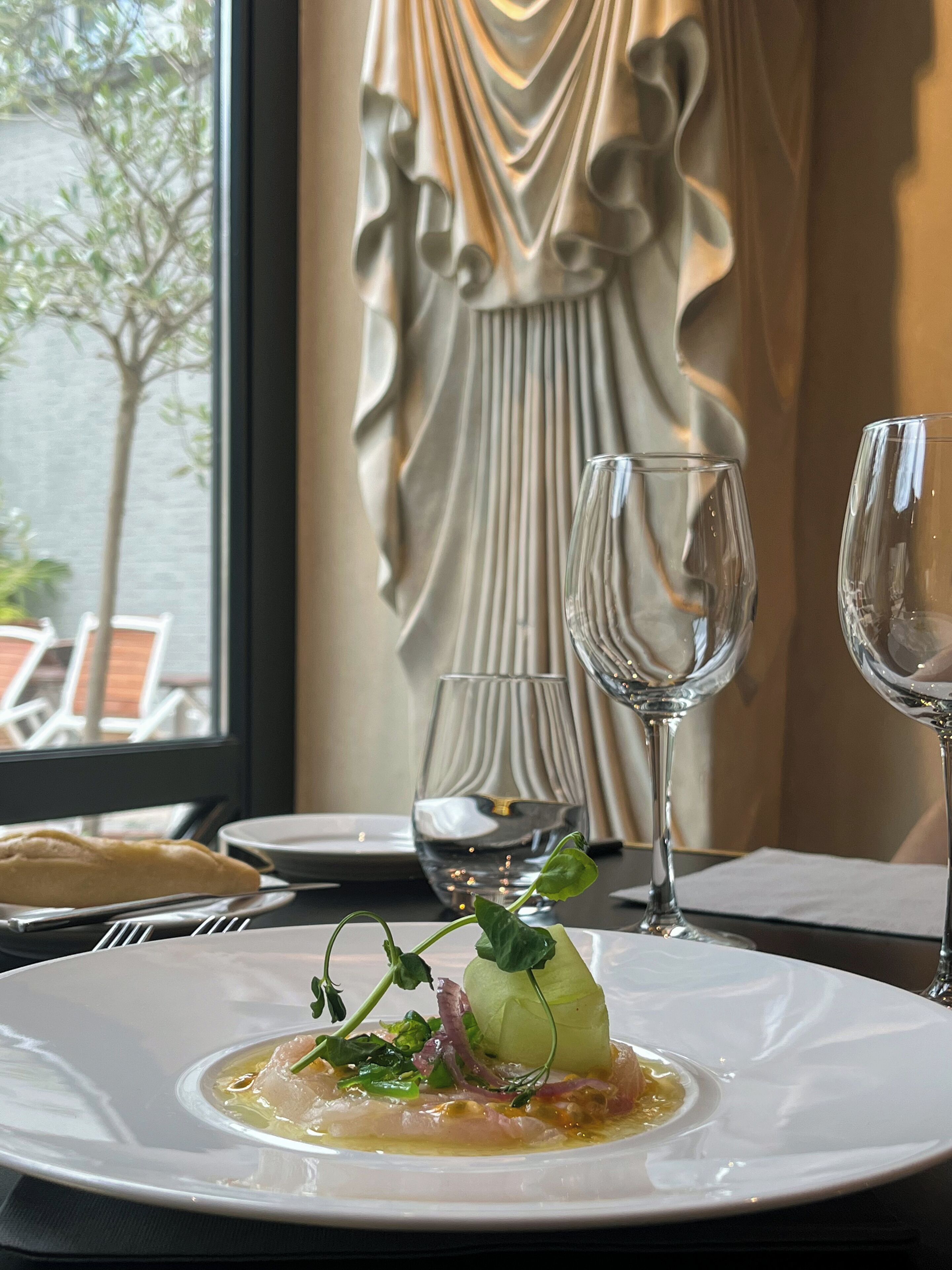 Une table à manger avec une assiette de nourriture, deux verres à vin et un rideau décoratif en arrière-plan.