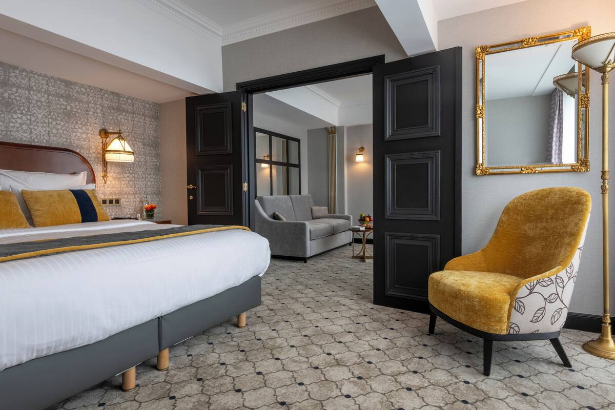 A hotel room with a bed, a sofa, a chair, a mirror, and a lamp.