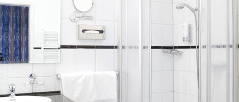 Un baño moderno con ducha de vidrio, un lavamanos con encimera oscura y un espejo sobre el lavamanos.