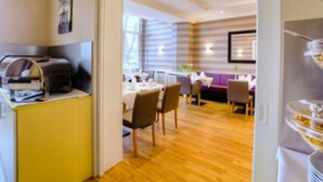 Una habitación de hotel con suelo de madera, un comedor con mesas y sillas, y una kitchenette con cafetera.