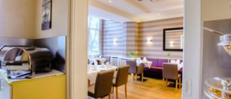 A hotel room with a wooden floor, a dining area with tables and chairs, and a kitchenette with a coffee machine.