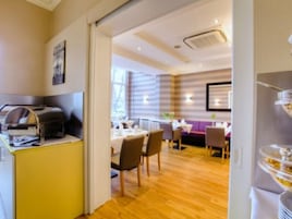 Ein Hotelzimmer mit Holzboden, einem Essbereich mit Tischen und Stühlen sowie einer Küchenzeile mit einer Kaffeemaschine.