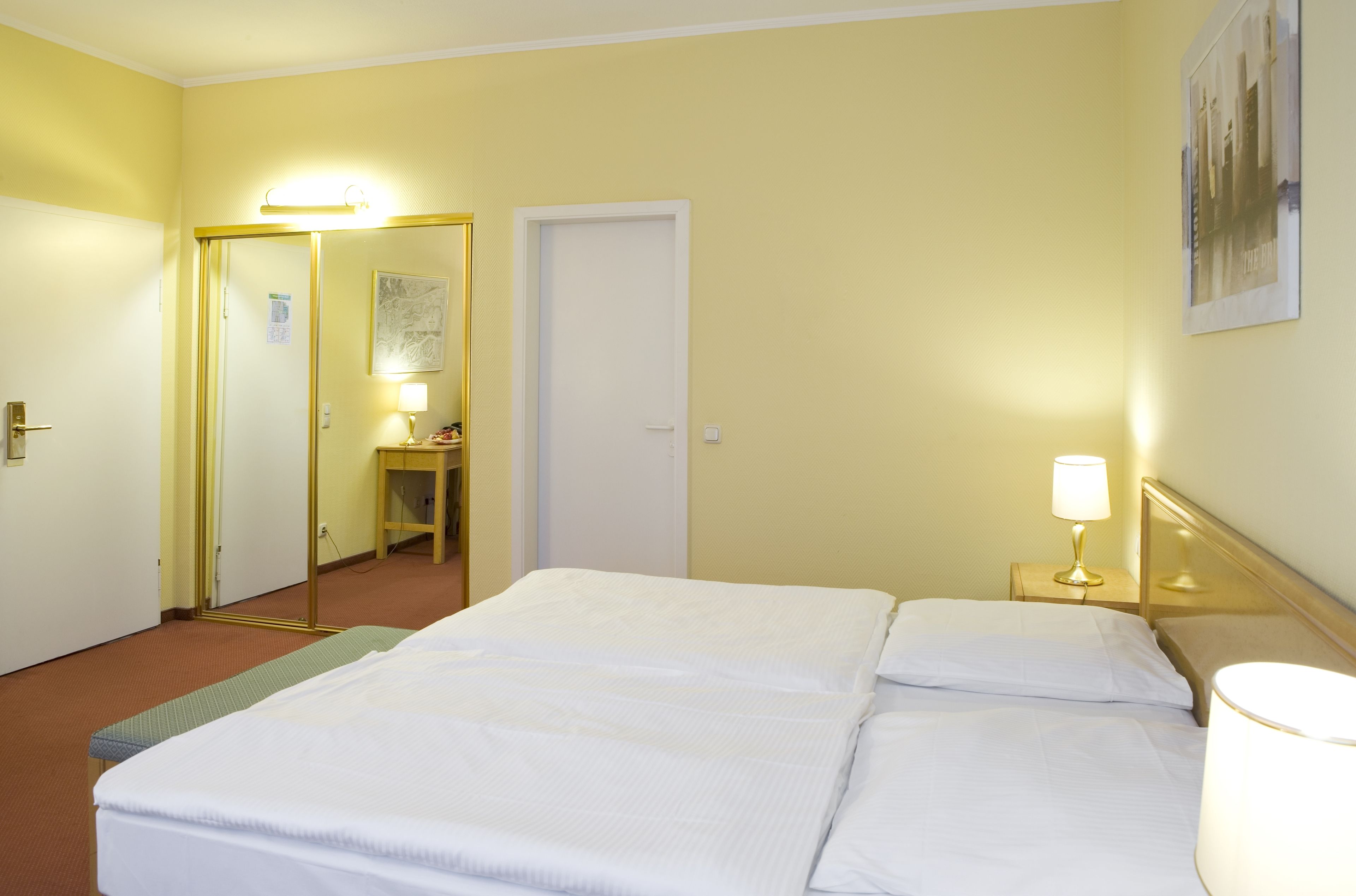 Une chambre d’hôtel avec un lit, des tables de chevet, un miroir et une porte.