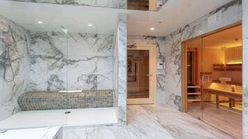 Un baño moderno con ducha envuelta en vidrio, paredes de mármol y un banco de madera.