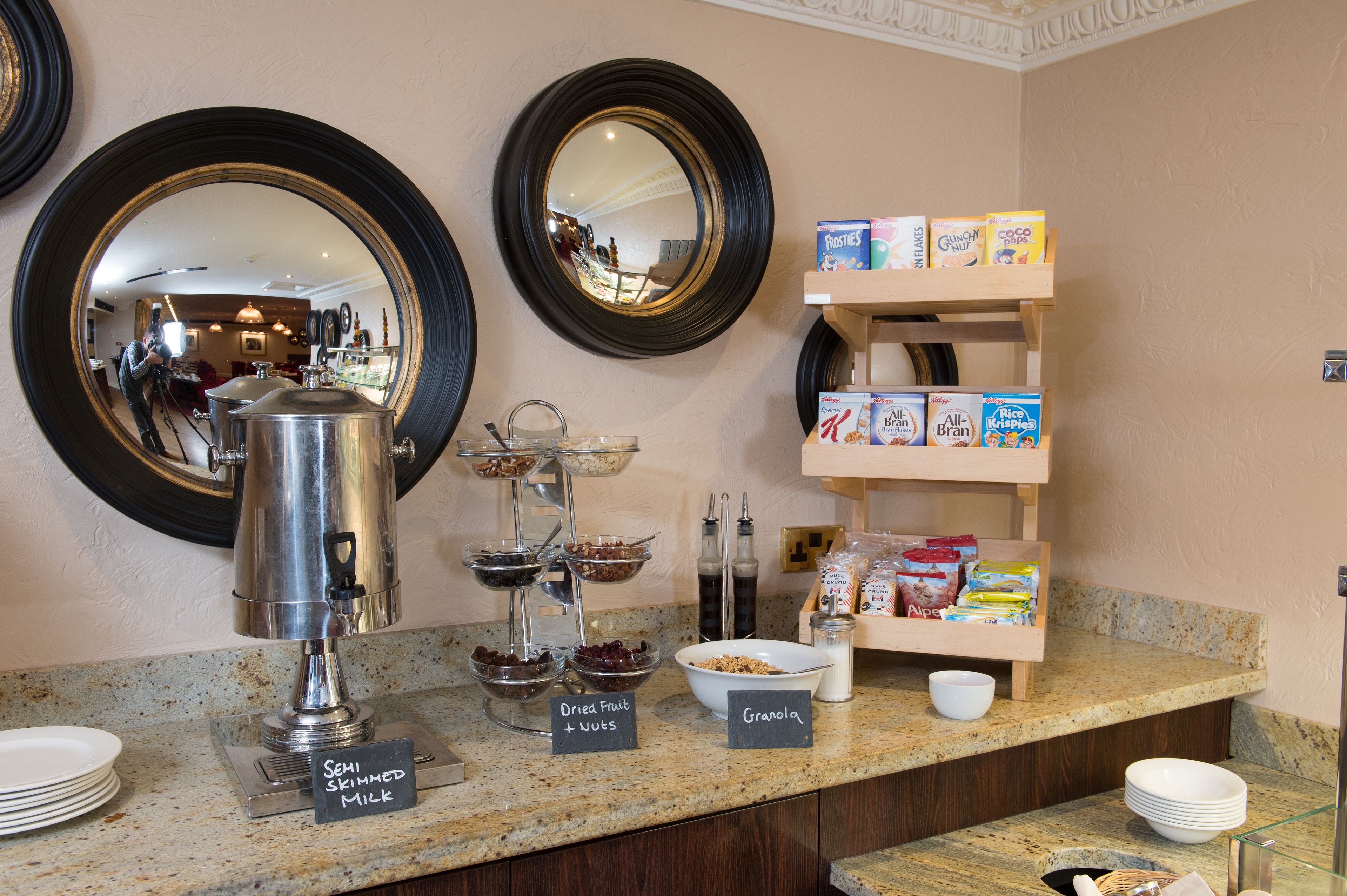 A breakfast buffet with a coffee pot, bowls of cereal, and a milk station.