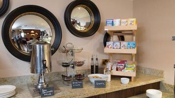 A breakfast buffet with a coffee pot, bowls of cereal, and a milk station.