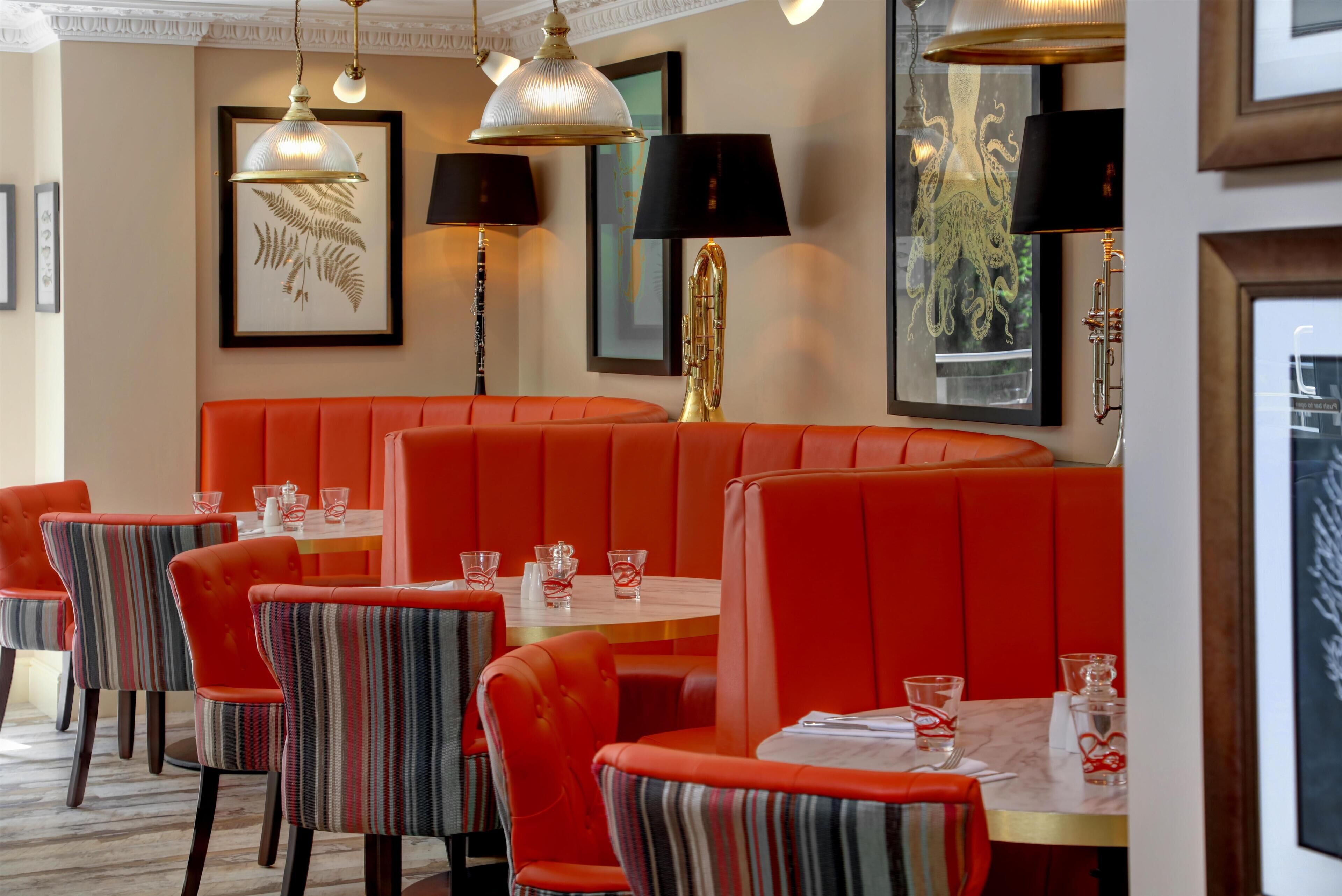A restaurant with red booths, striped chairs, and framed artwork on the walls.
