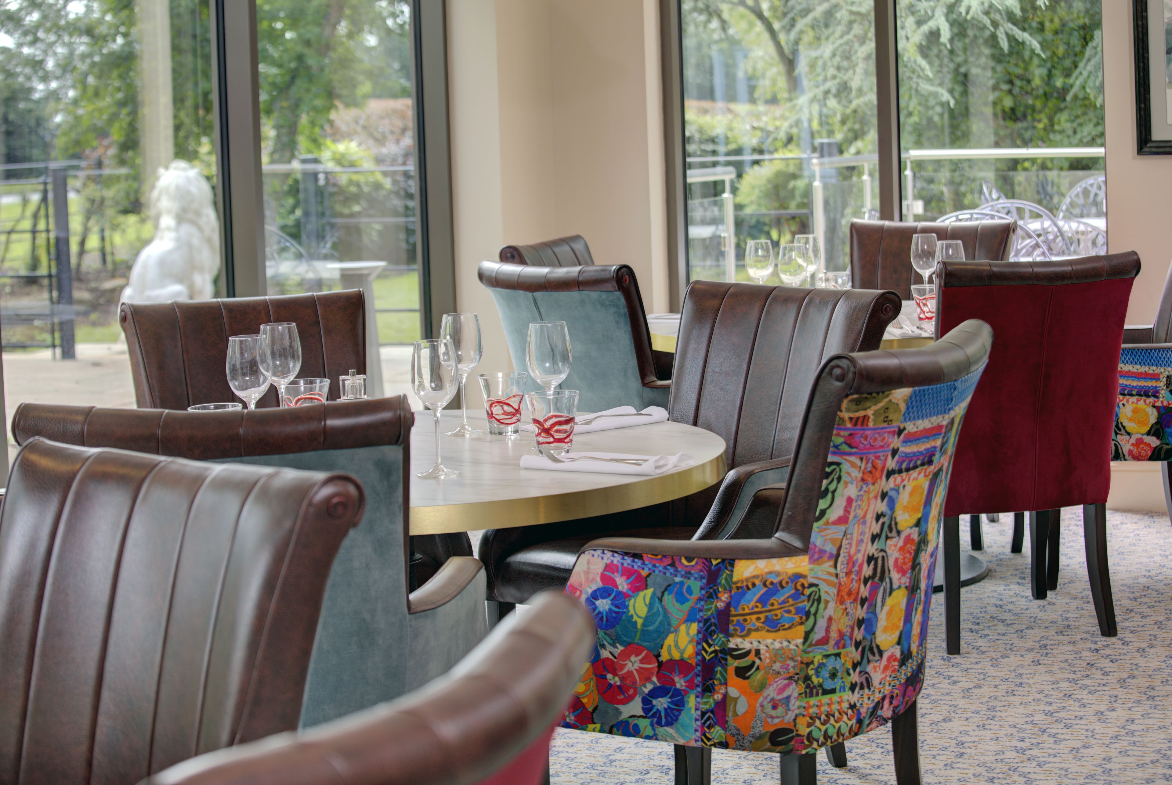 A dining area with leather chairs, a round table, and a view of greenery outside.