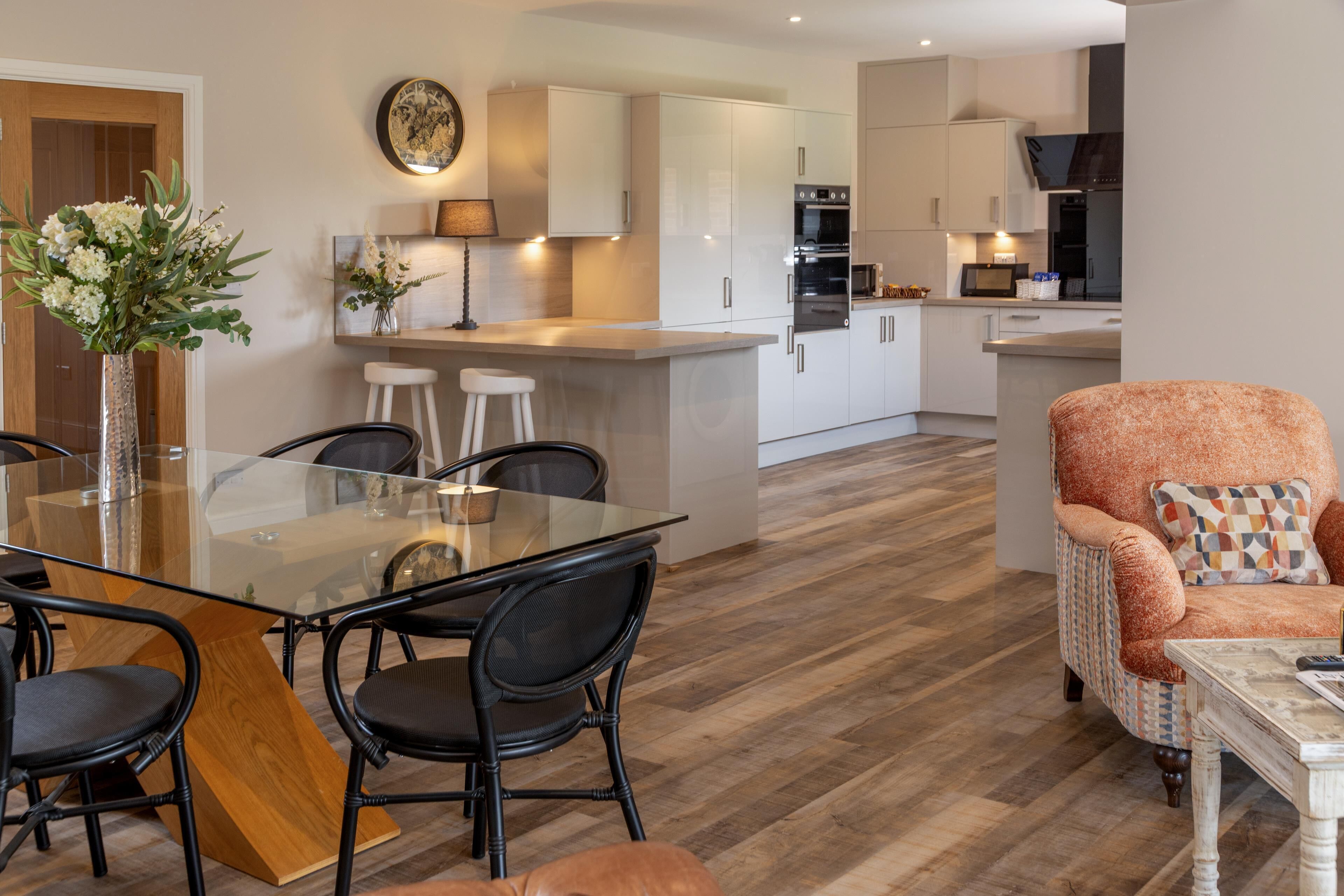 A modern kitchen with white cabinets, a central island, and a dining area with a glass table and black chairs.