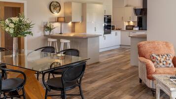 A modern kitchen with white cabinets, a central island, and a dining area with a glass table and black chairs.