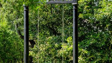 A swing set with a metal frame and chains, surrounded by lush greenery and trees.