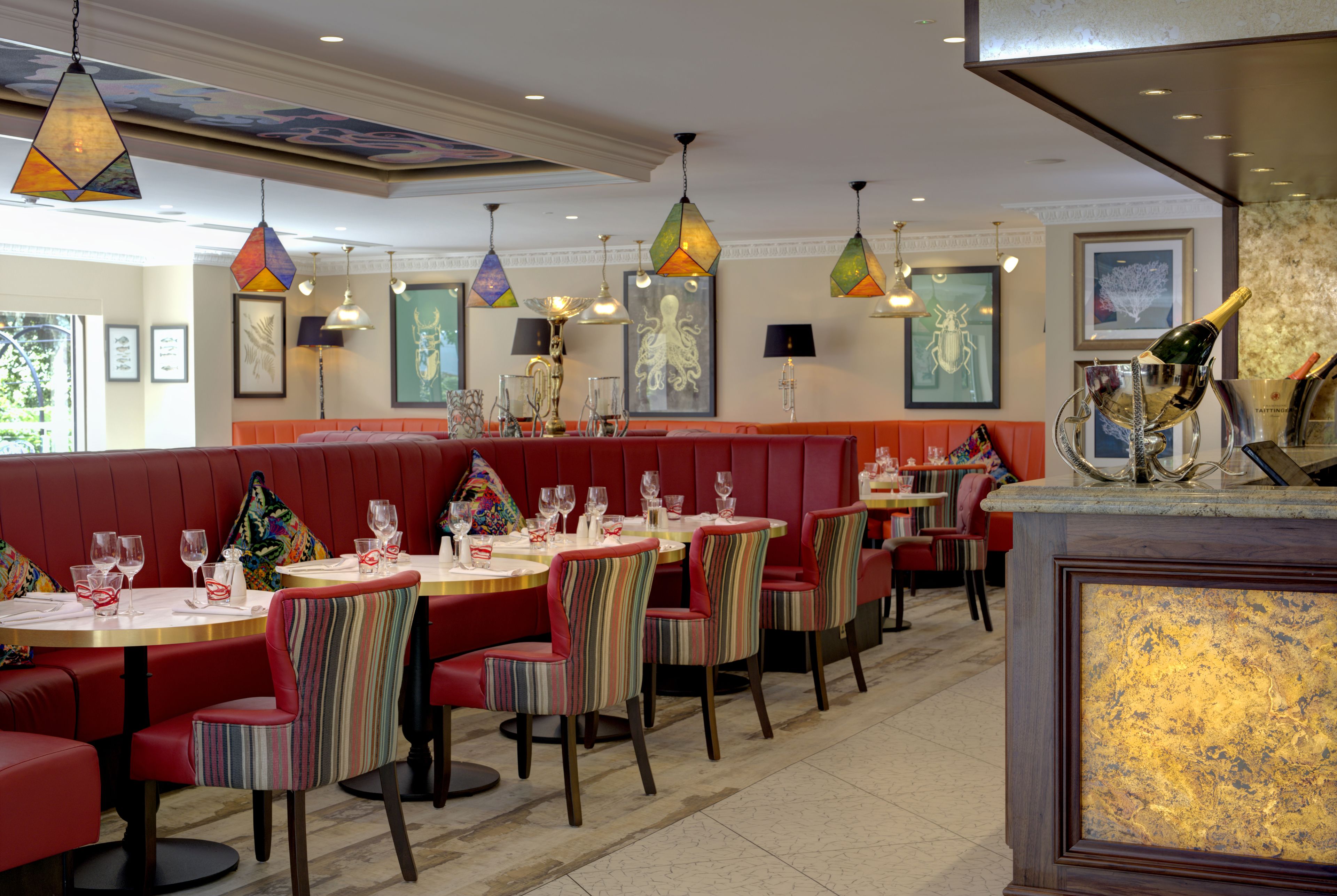 Een restaurant met zitjes en ronde tafels, met kleurrijke gestreepte stoelen en hanglampen.