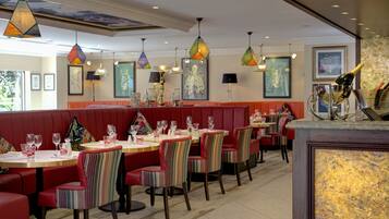 Een restaurant met zitjes en ronde tafels, met kleurrijke gestreepte stoelen en hanglampen.