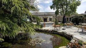 Un cortile con uno stagno, panchine in pietra e un edificio con un grande albero e una statua.