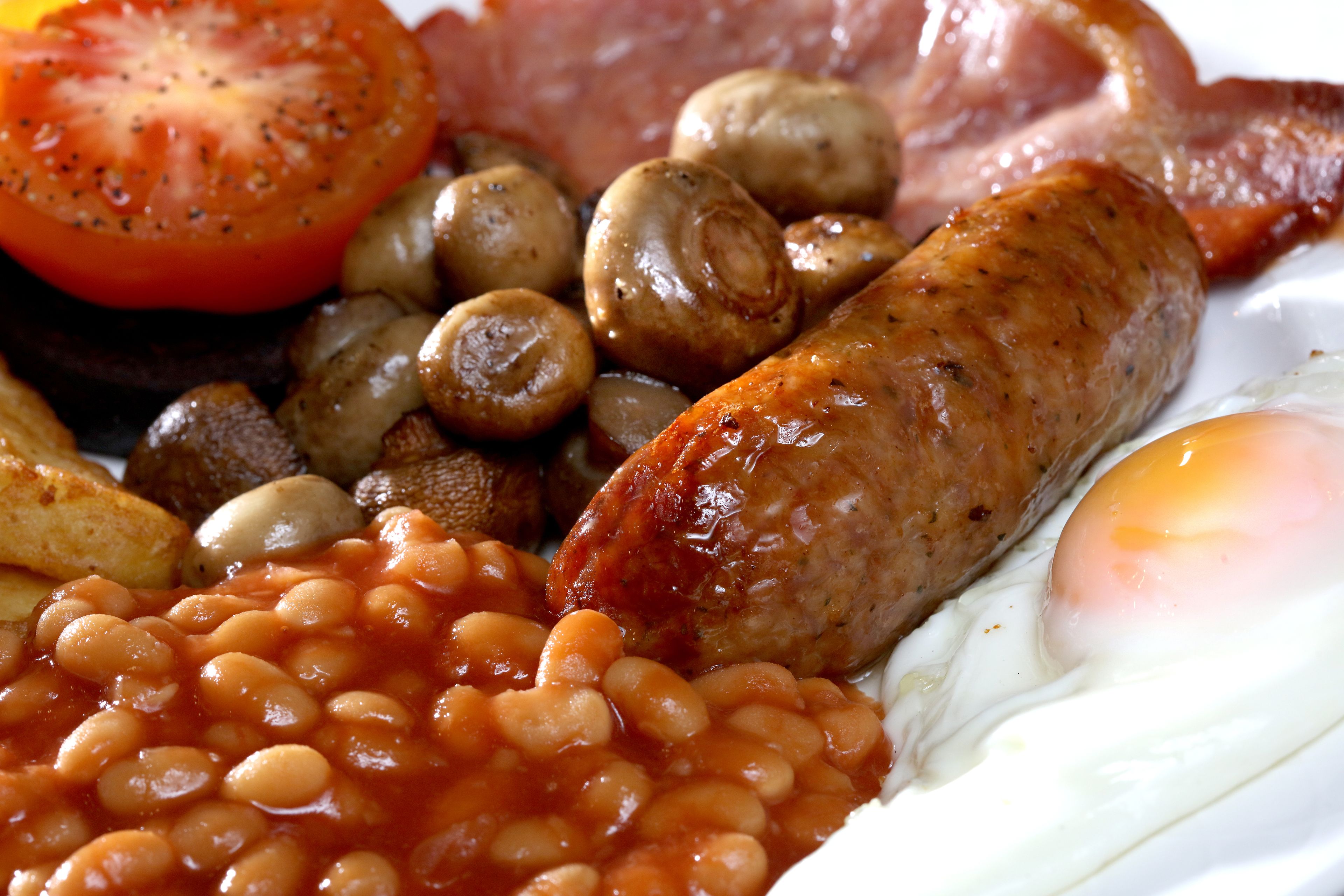 A breakfast plate with eggs, sausages, mushrooms, baked beans, bacon, and a tomato.