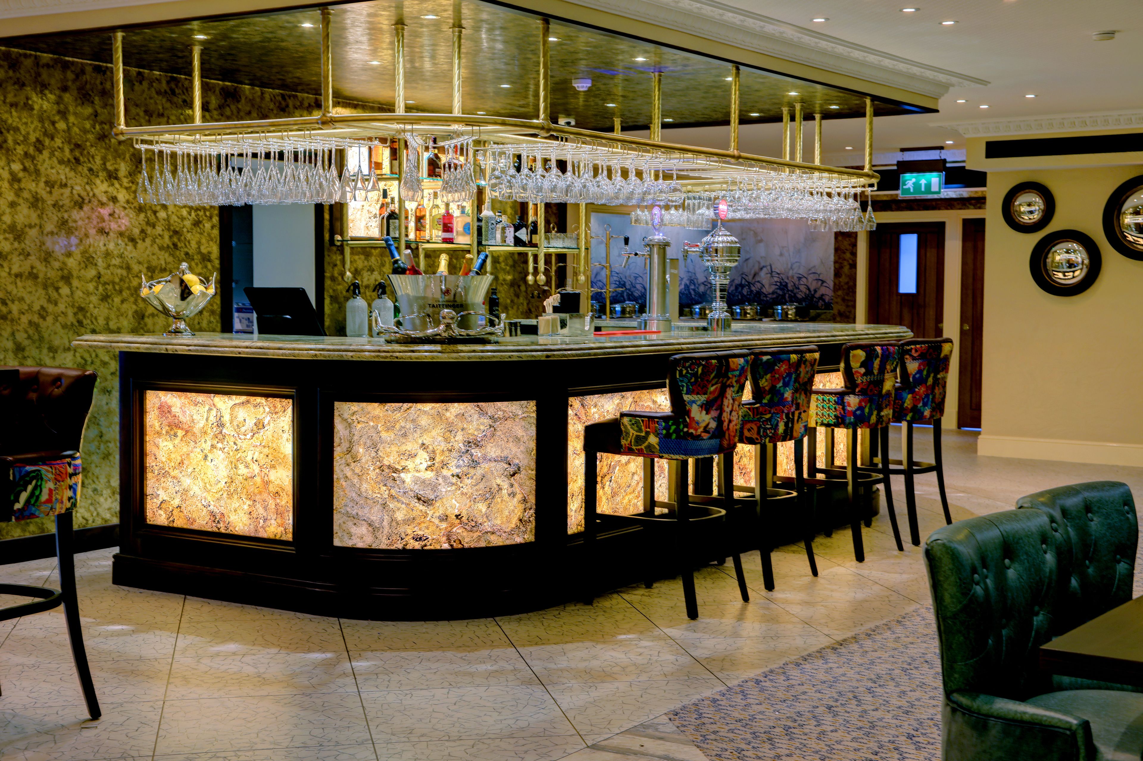 A bar area with a marble countertop, bar stools, and a chandelier.