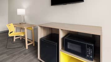 Ett kompakt hotellrum med ett skrivbord, en stol, en platt-TV och inbyggda vitvaror, inklusive ett kylskåp och en mikrovågsugn.