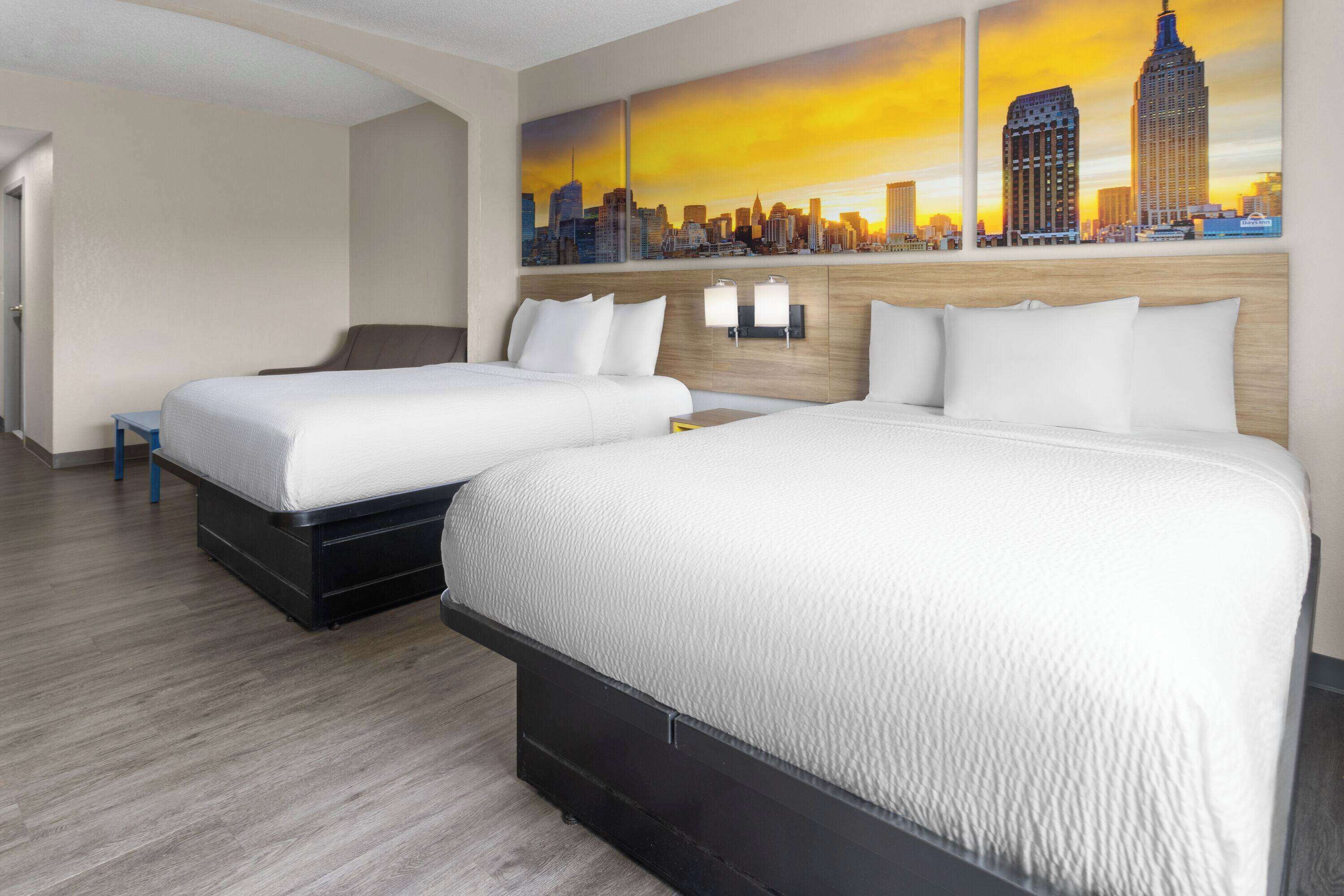 A hotel room with two beds, a cityscape mural on the wall, and a wooden floor.