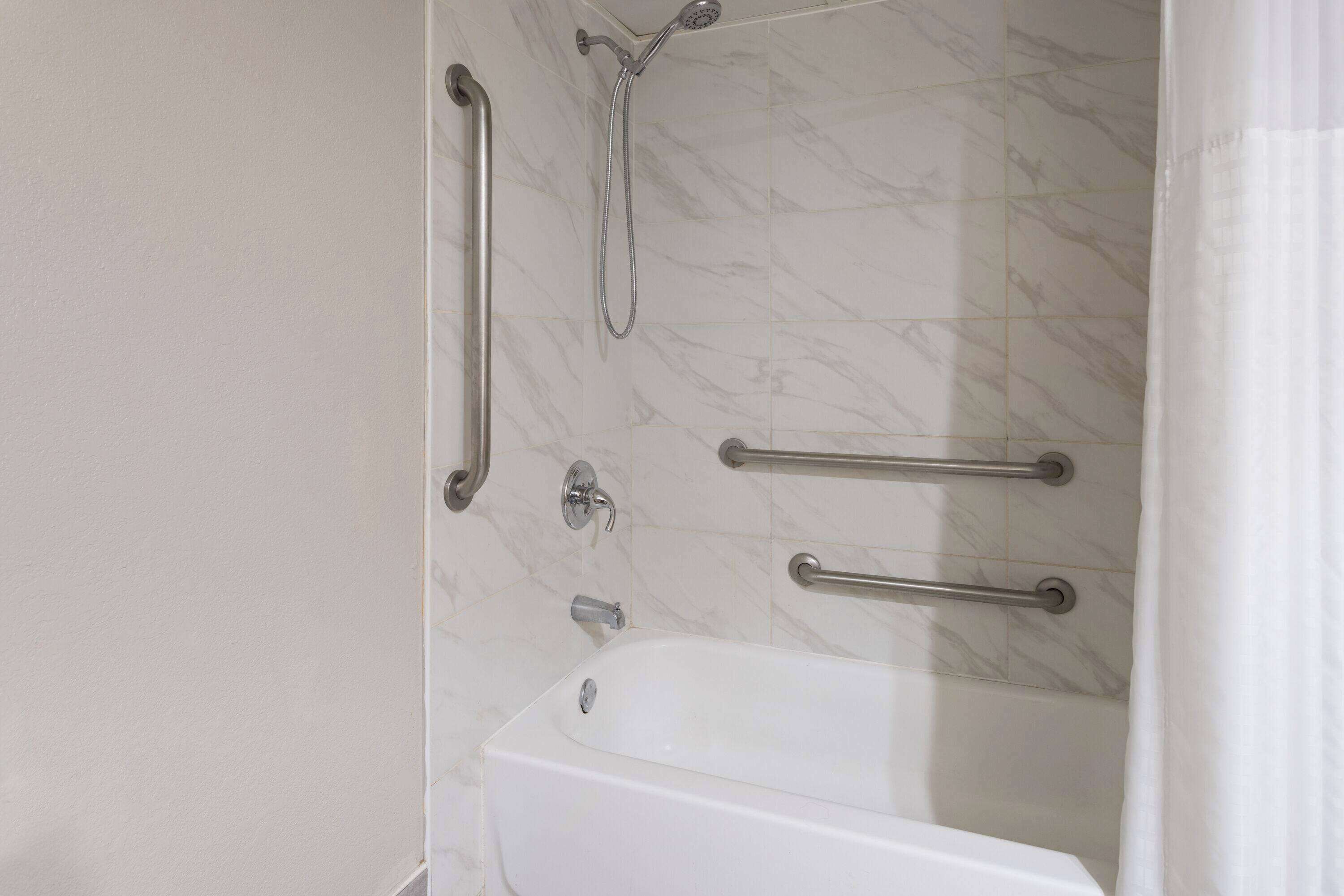 A bathroom with a white bathtub, a shower with a handheld showerhead, and two grab bars on the wall.