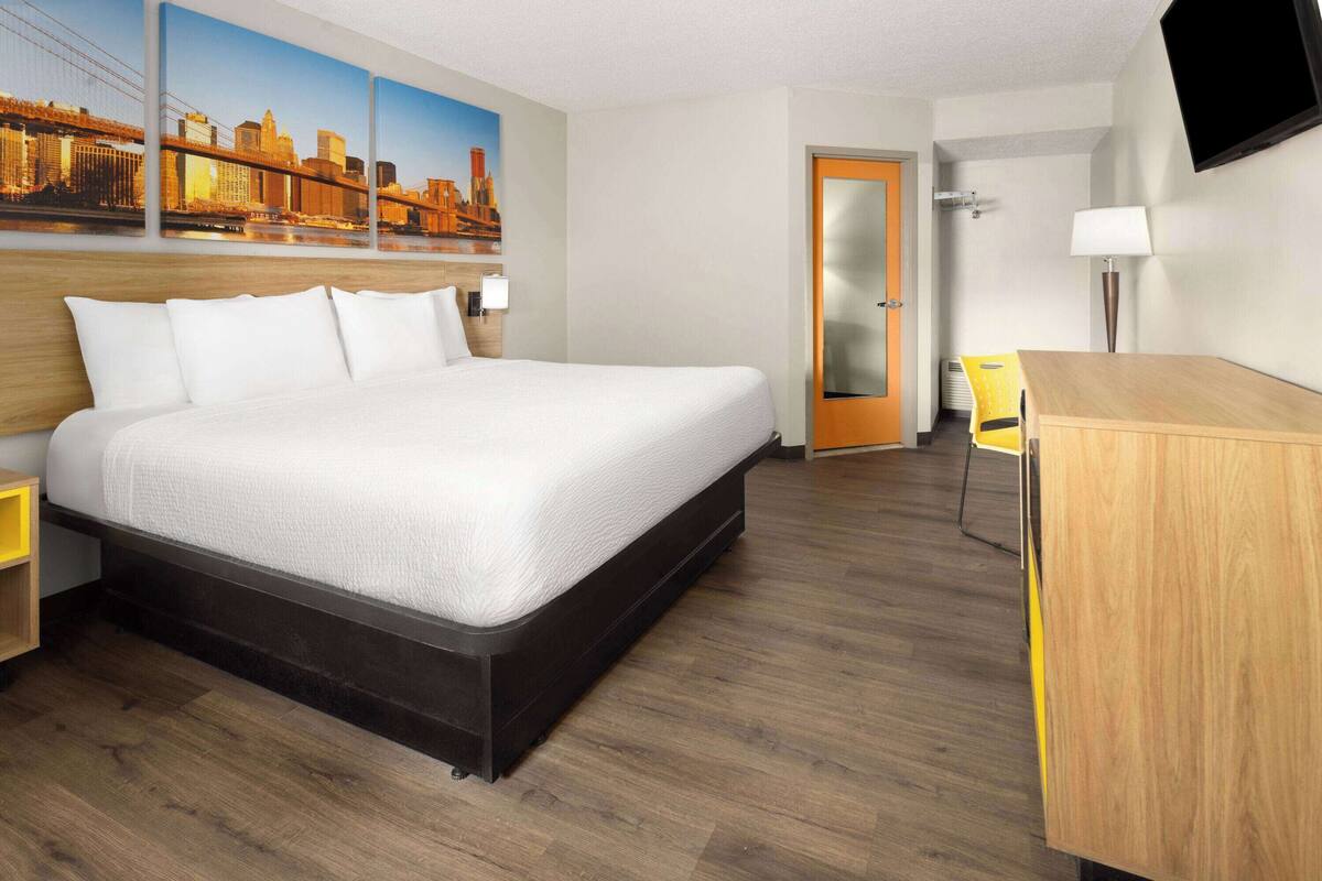 Habitación de hotel con una cama grande, un escritorio, una silla, un televisor fijado a la pared y una puerta.