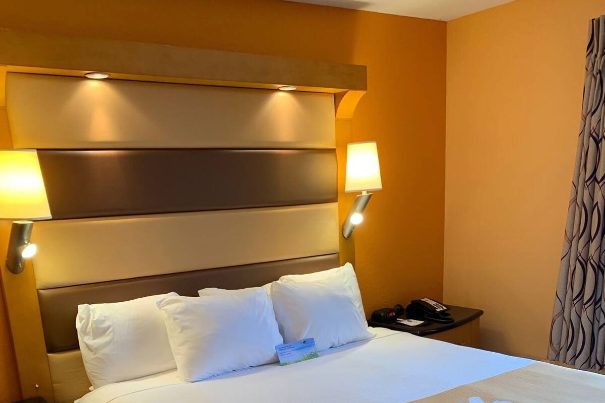 Habitación de hotel con cama, lámparas de noche, mesita de noche y colcha con el estampado 'Hello Sunshine'.