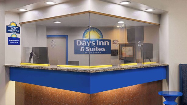 A reception desk with a blue and brown color scheme, a sign for Days Inn & Suites, and a check-in time sign.