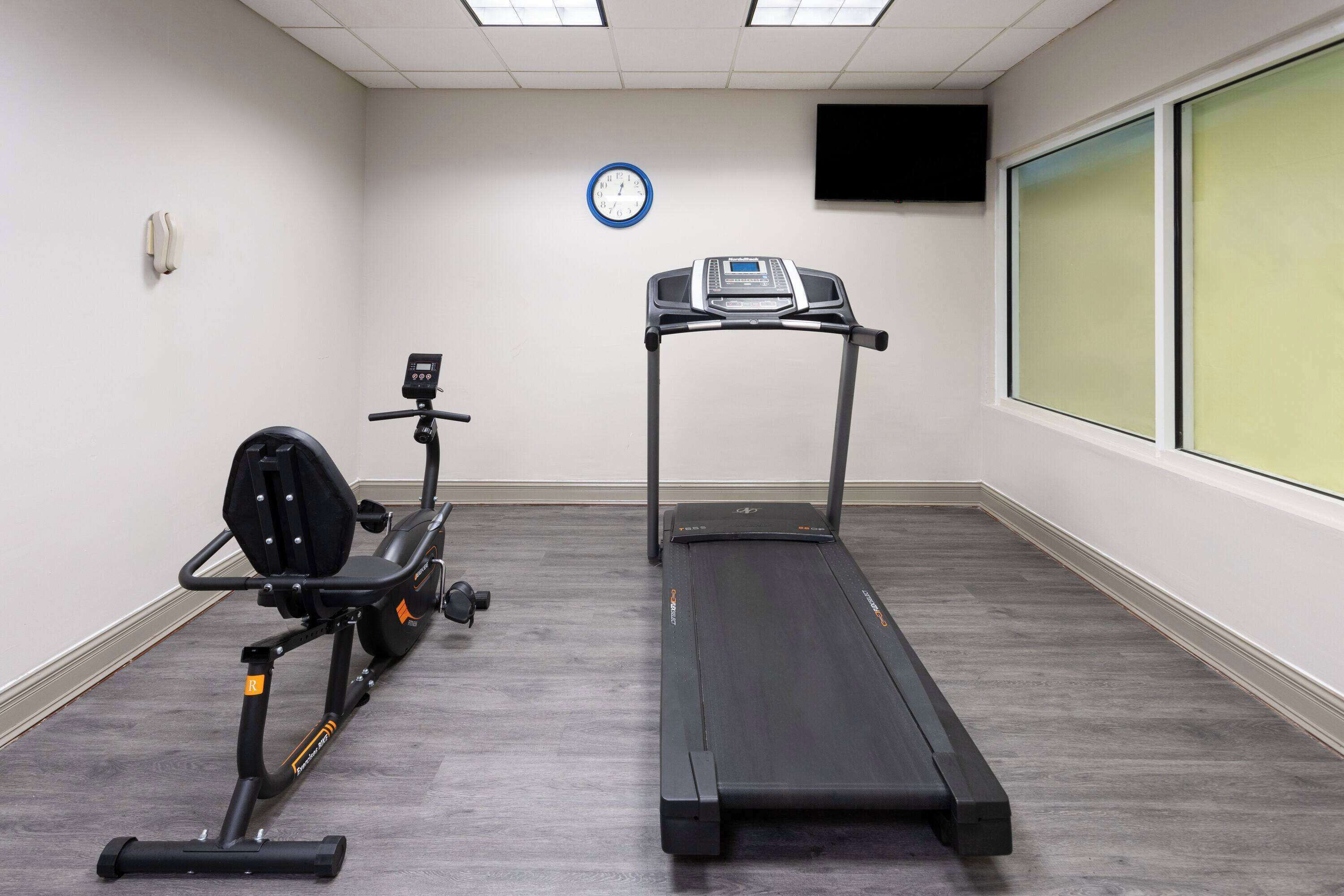 A room with a treadmill, an elliptical, a clock, and a TV on the wall.